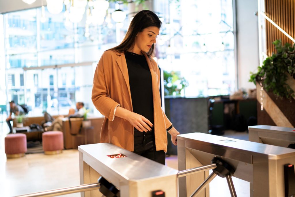 a woman scans an access reader on a turnstile in an office building with her access card